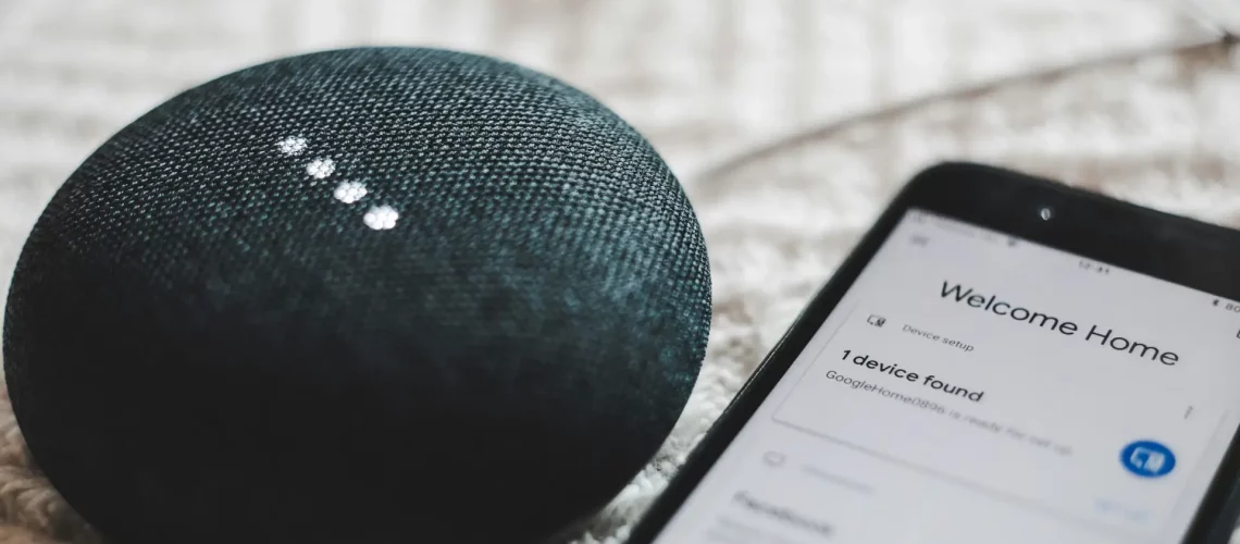 turned-on charcoal Google Home Mini and smartphone